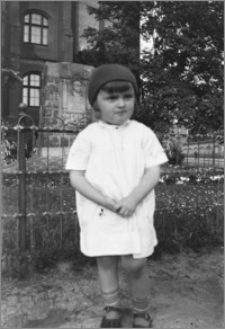 [Portret kilkuletniej dziewczynki stojącej na tle obelisku Stefana Łaszewskiego na skwerku przy gmachu Pomorskiego Urzędu Wojewódzkiego w Toruniu]