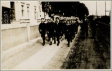 Czesław Bartkowiak z grupą chłopców i mężczyzną maszerują ulicami miasta